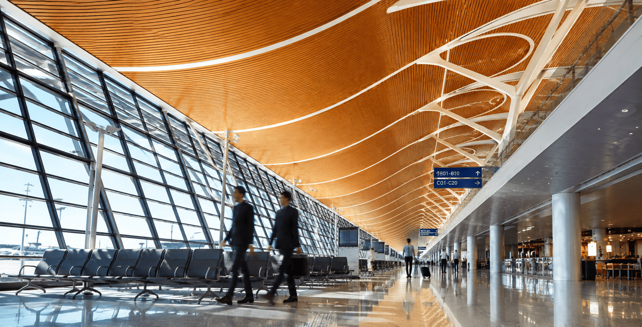 Modern interior of Shanghai Pudong International Airport (PVG) Terminal showing passengers walking under a wave-shaped wooden ceiling design near departure gates.